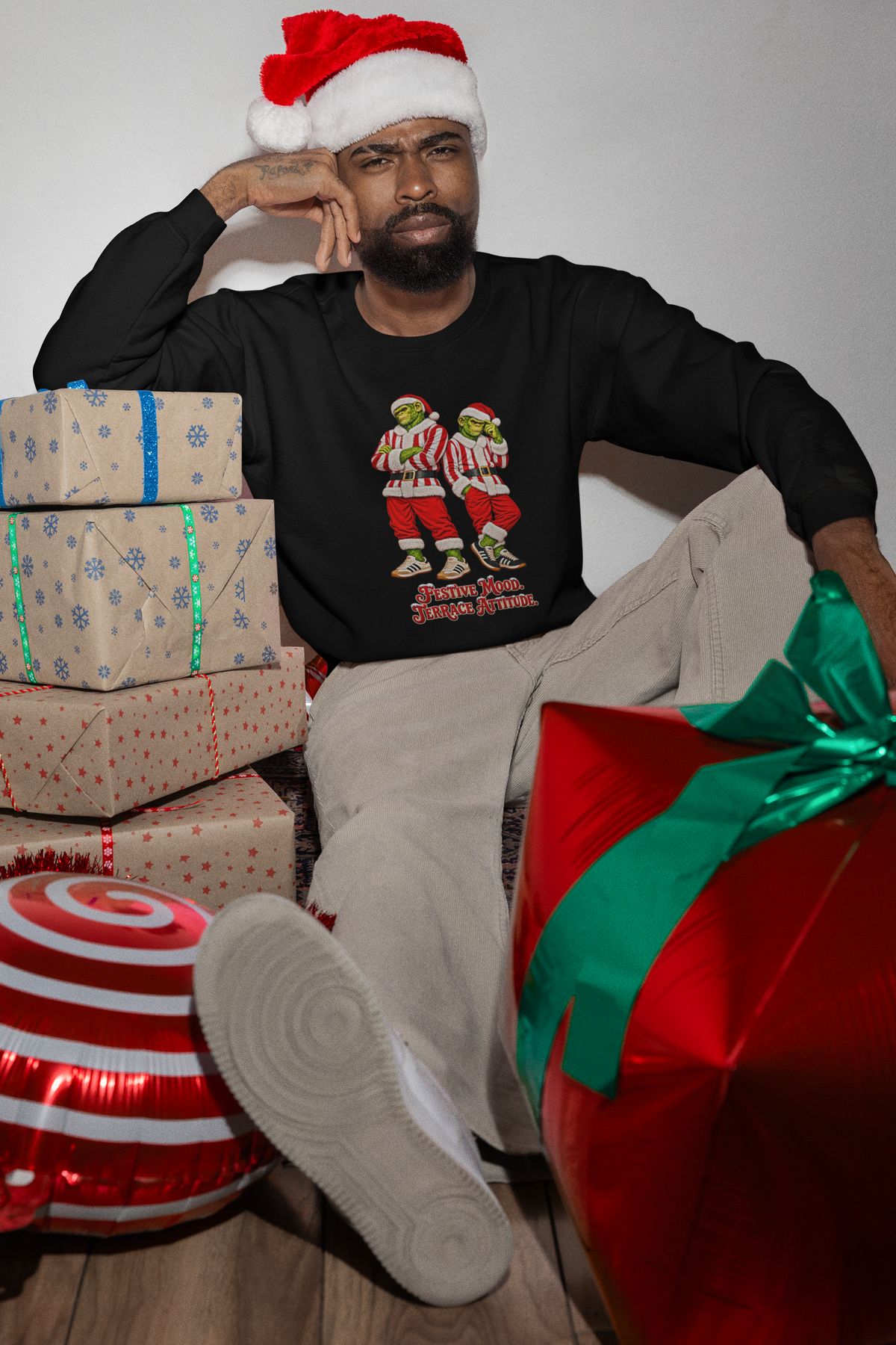 Man in a Santa hat by wrapped presents wearing the red and white stripe Northern Monkeys jumper