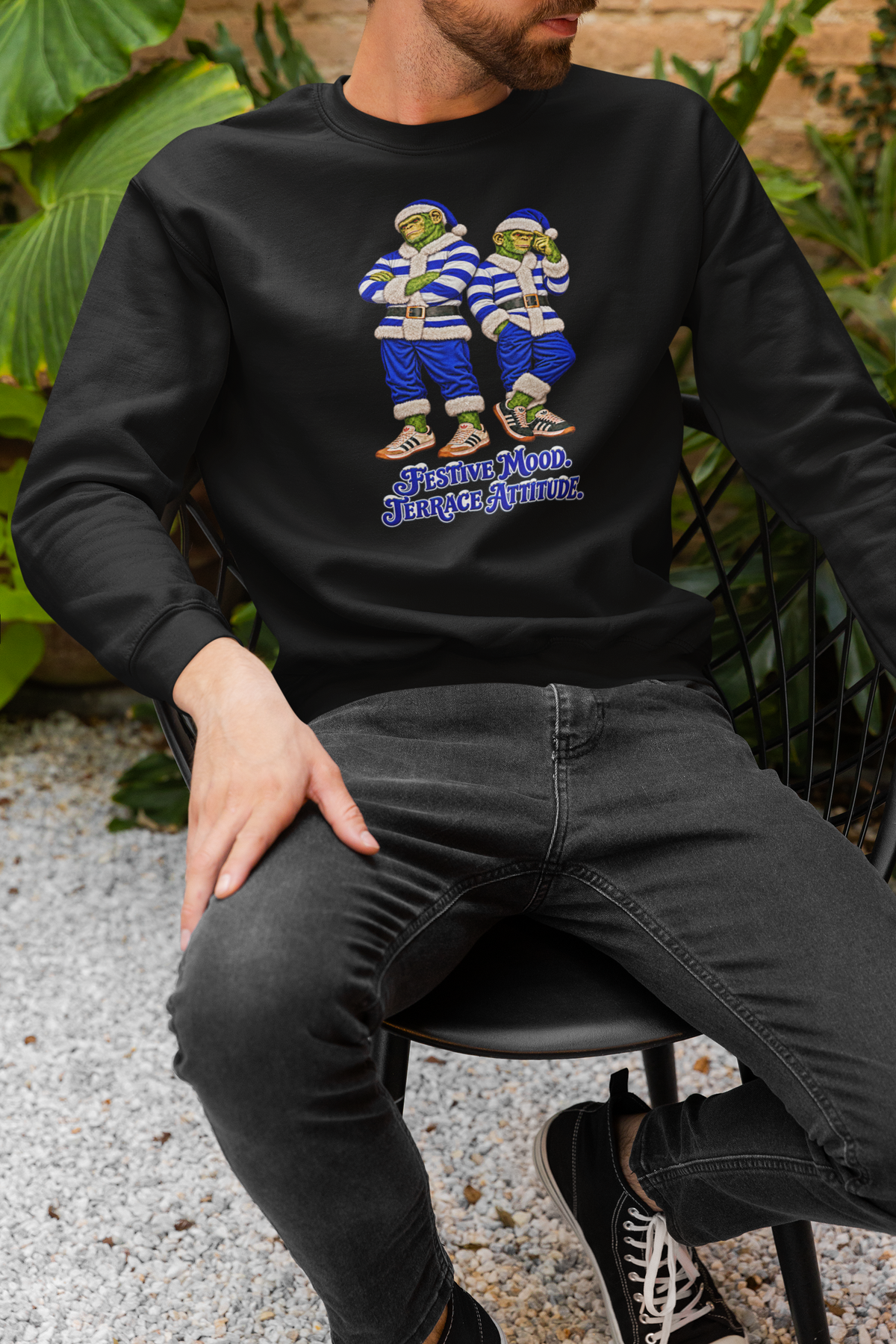 Man sitting on a chair outdoors wearing the blue and white hooped Northern Monkeys Christmas jumper
