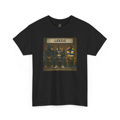 A black short-sleeve crewneck Leeds t-shirt featuring a rectangular graphic print on the chest. The graphic shows three hooded figures sitting on a bench, with a banner above them reading 'LEEDS'.