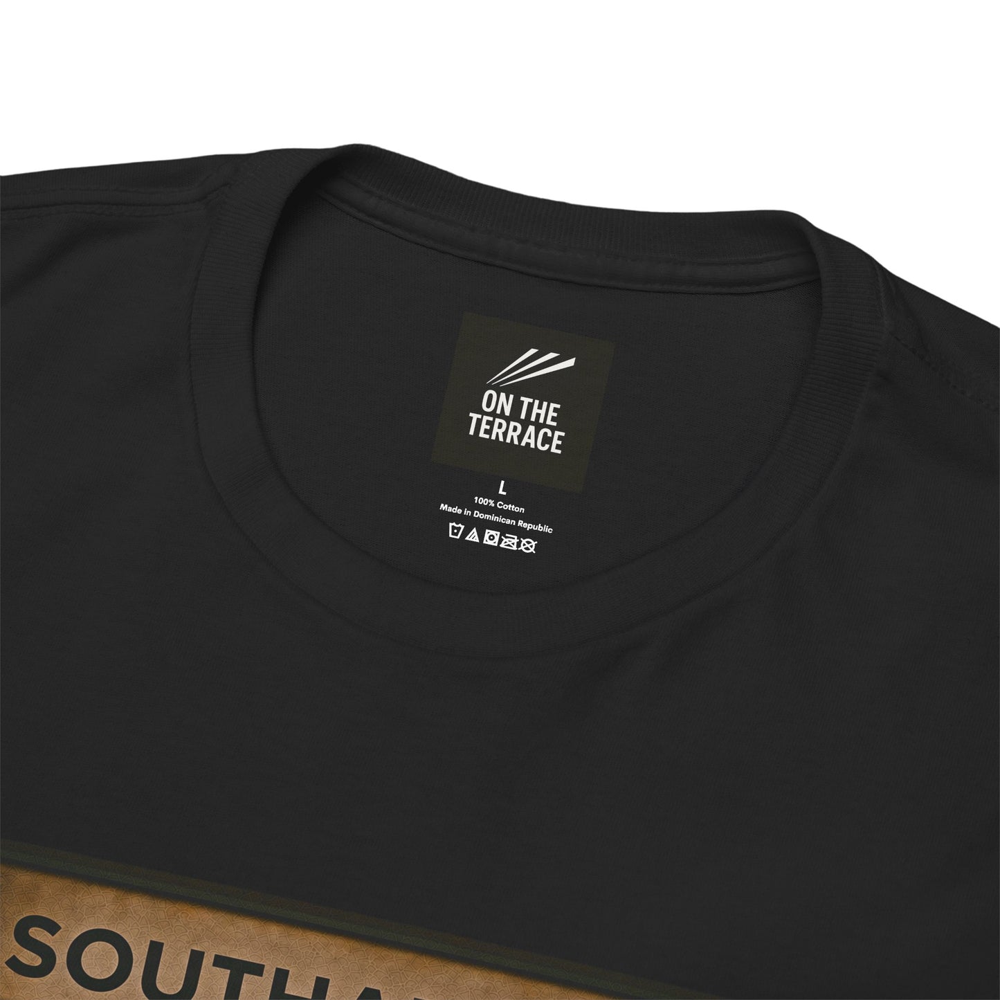 Close-up of a black short-sleeve Southampton t-shirt showing the inner neck label which reads 'ON THE TERRACE' and a brown cardboard box edge with 'SOUTH A' printed on it.