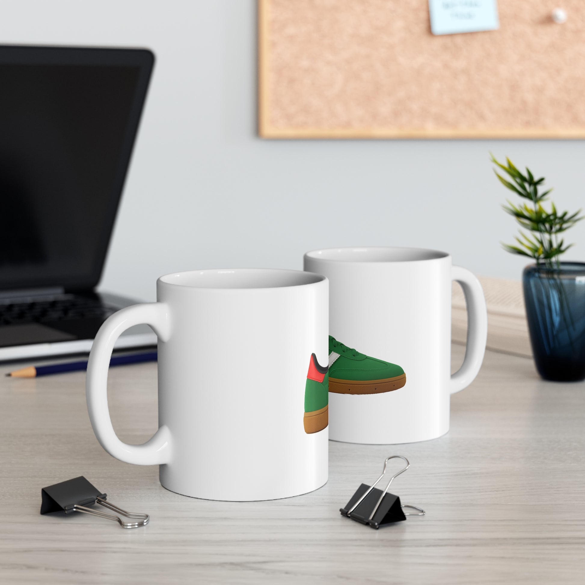 White ceramic mugs with green and brown sneaker design on office desk with laptop and plant