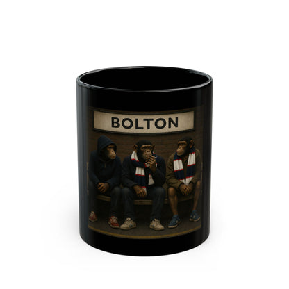 A high-gloss black ceramic mug features a rectangular graphic of three chimpanzees dressed as 1980s football casuals sitting on a railway platform bench. Above them hangs a vintage cream station sign with the word "BOLTON" in black capital letters. The monkeys wear casual coats, hoodies, retro low-profile trainers, and navy, white, and red striped bar scarves against a brick wall background.