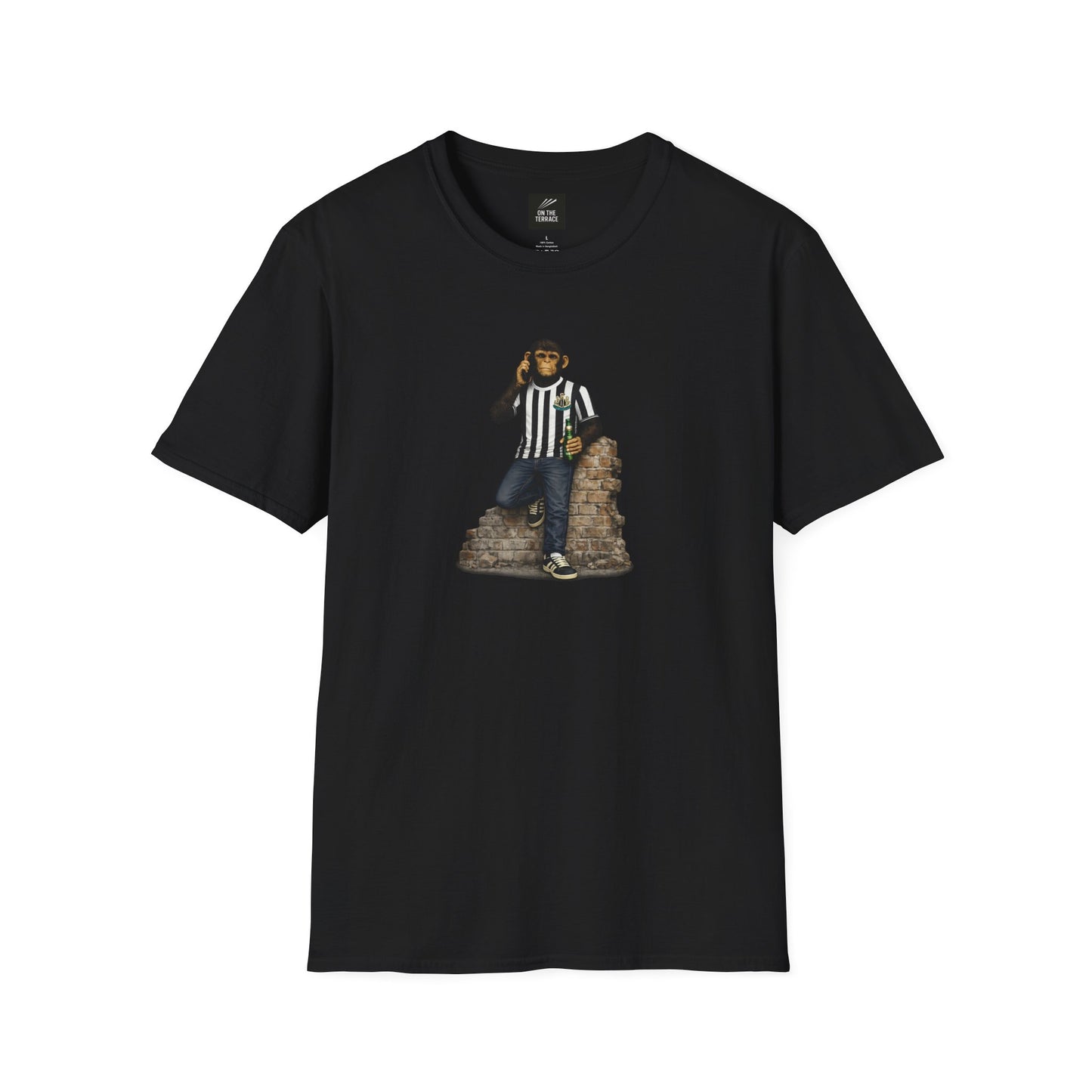 A black short-sleeved crew-neck t-shirt featuring a central graphic of a chimpanzee dressed in a black and white striped football jersey, denim jeans, and black trainers. The character is leaning against a section of a brick wall while holding a green bottle and talking on a mobile phone.