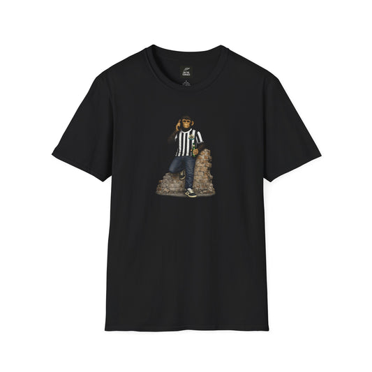 A black short-sleeved crew-neck t-shirt featuring a central graphic of a chimpanzee dressed in a black and white striped football jersey, denim jeans, and black trainers. The character is leaning against a section of a brick wall while holding a green bottle and talking on a mobile phone.