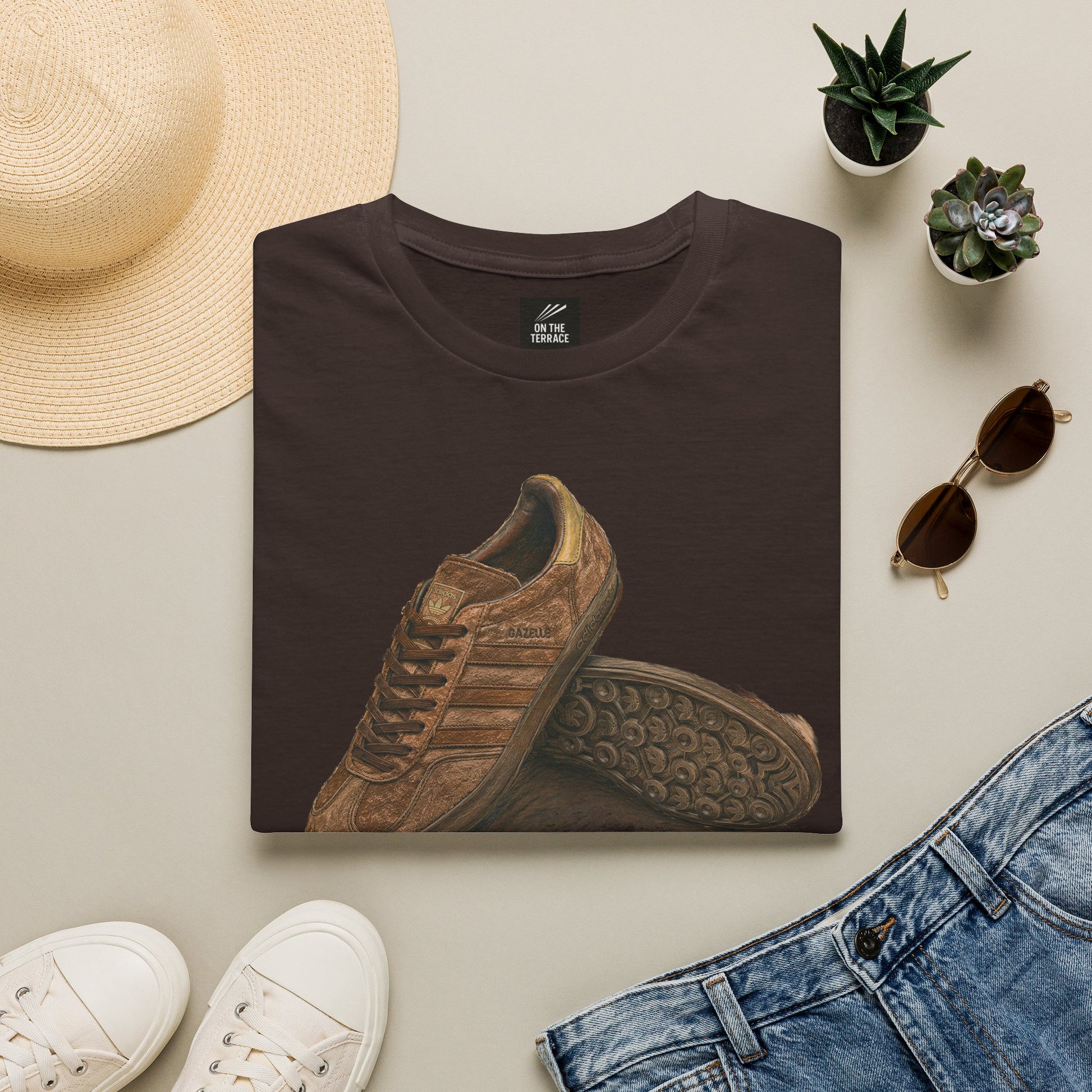 Brown t-shirt with shoe design, white sneakers, straw hat, sunglasses, and jeans on a light gray background.