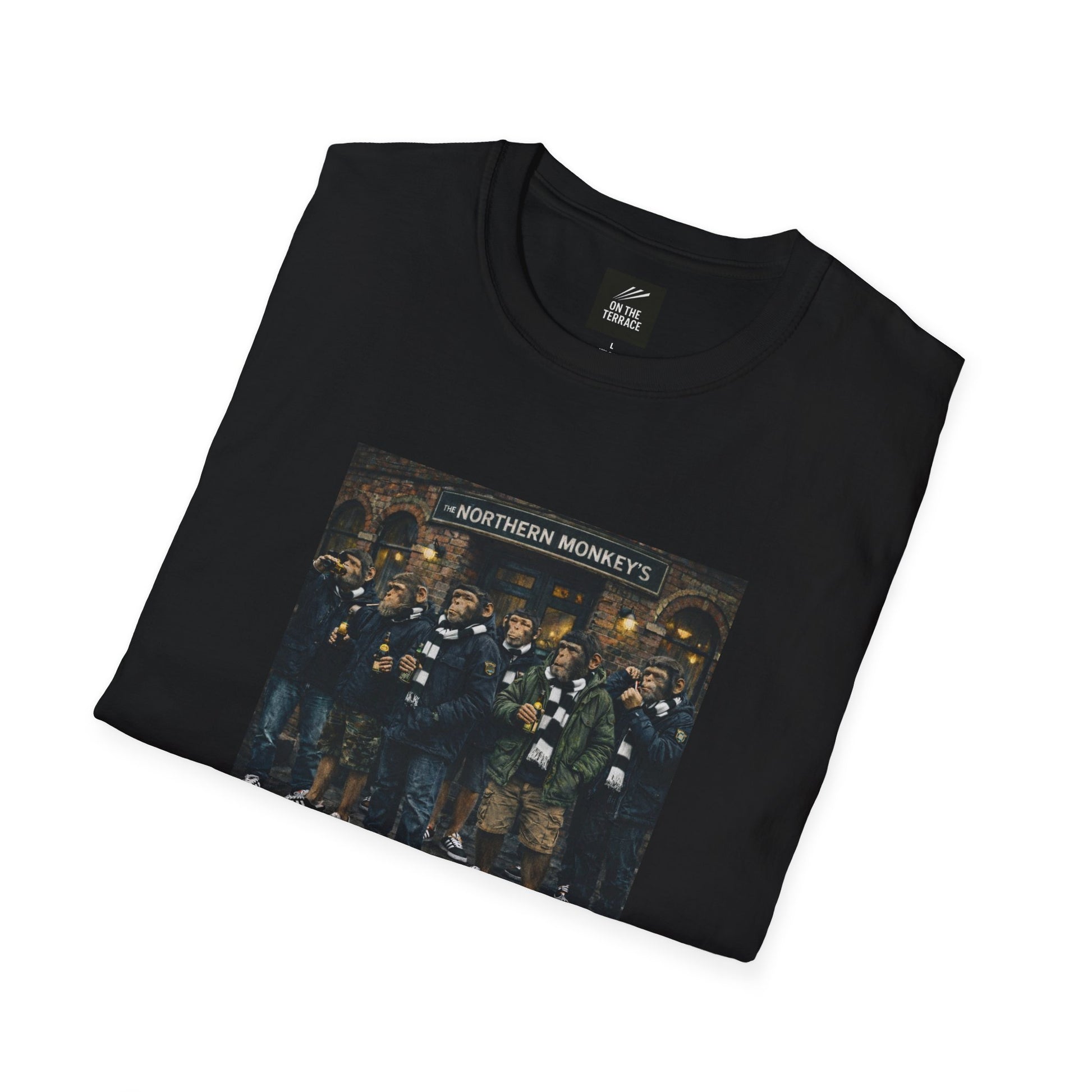 A front-facing view of a black crewneck t-shirt featuring a central graphic illustration. The artwork depicts seven chimpanzees dressed in British "terrace culture" fashion—wearing olive and navy parkas, puffer jackets, black-and-white striped scarves, and black trainers. They are gathered in front of a traditional brick pub with a sign that reads "THE NORTHERN MONKEY'S."