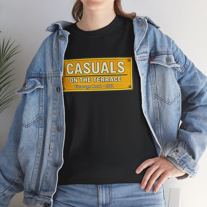 A person wearing a black Watford T-shirt under an open light-wash denim jacket, paired with blue jeans. The T-shirt features a yellow street-sign style graphic reading 'CASUALS ON THE TERRACE' with smaller text below.