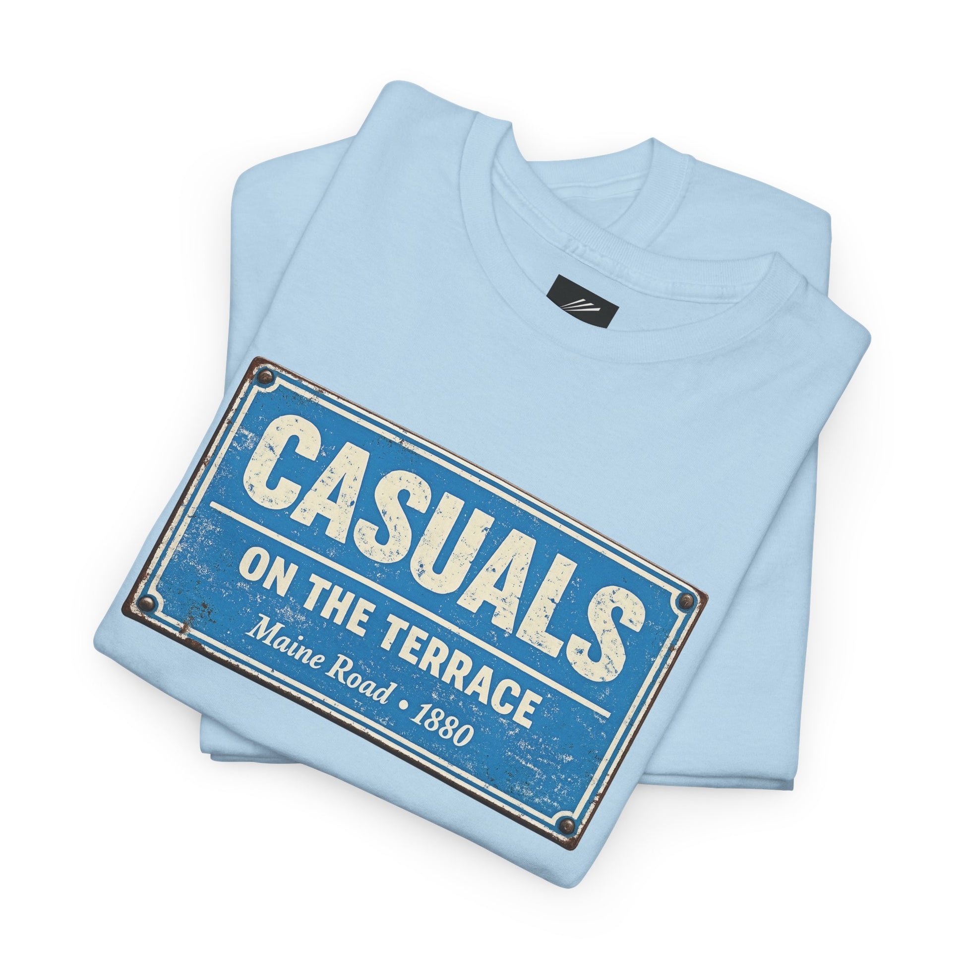 A light blue folded MCFC t-shirt featuring a central vintage blue and white street sign graphic reading "CASUALS ON THE TERRACE" with "Maine Road • 1880" printed below, and an inner neck label for On The Terrace. on a white background.