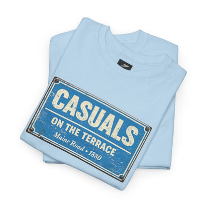 A light blue folded MCFC t-shirt featuring a central vintage blue and white street sign graphic reading "CASUALS ON THE TERRACE" with "Maine Road • 1880" printed below, and an inner neck label for On The Terrace. on a white background.
