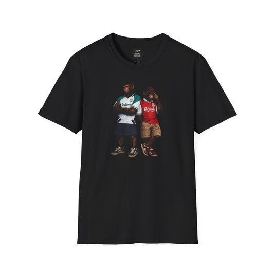 A black short-sleeved t-shirt featuring a central graphic of two chimpanzees dressed as Liverpool FC supporters. The chimpanzee on the left stands with arms crossed, wearing the iconic 1995-96 green and white quartered away jersey with the "Carlsberg" sponsor. The chimpanzee on the right wears a classic red Liverpool home kit, khaki cargo shorts, a burgundy bucket hat, and burgundy terrace-style trainers. Both figures are rendered in a detailed, realistic painting style against the solid black fabric. 