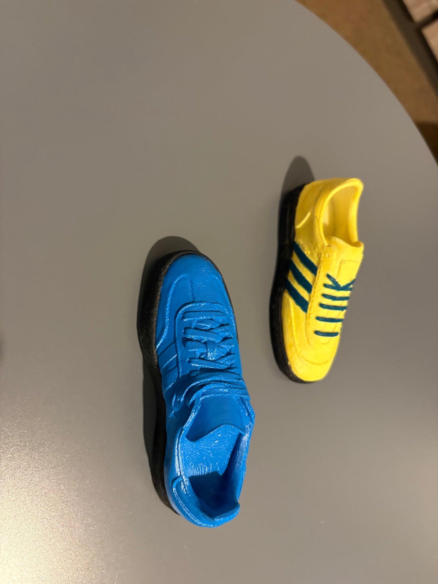 Miniature football casual shoes in blue and yellow with black soles on gray surface
