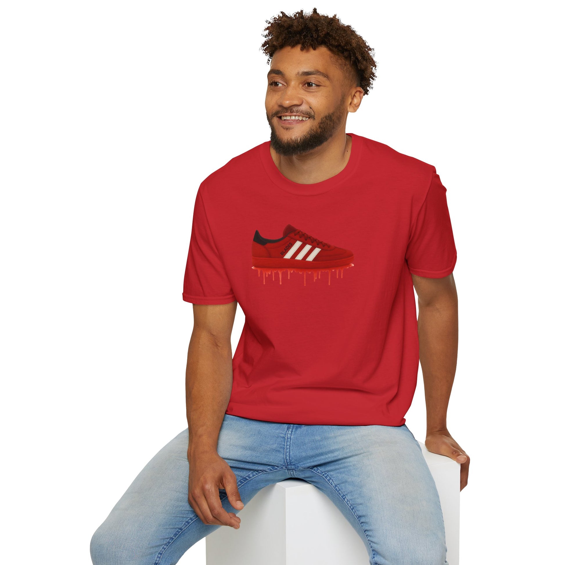 Smiling man wearing red graphic t-shirt with dripping red sneaker print and light blue jeans sitting on white cube