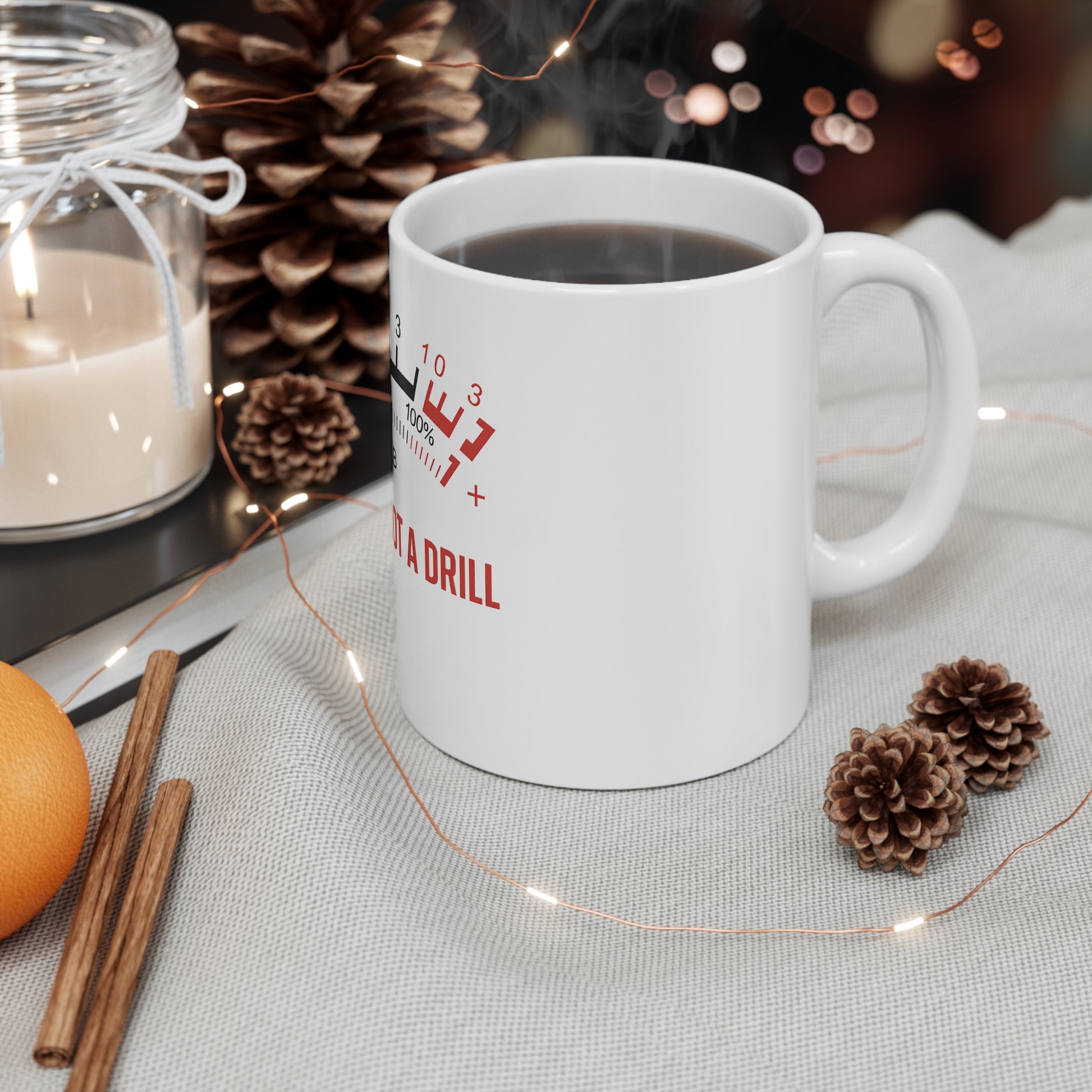 White coffee mug with combustion gauge and text on gray fabric, pine cones, candle, orange, and cinnamon sticks
