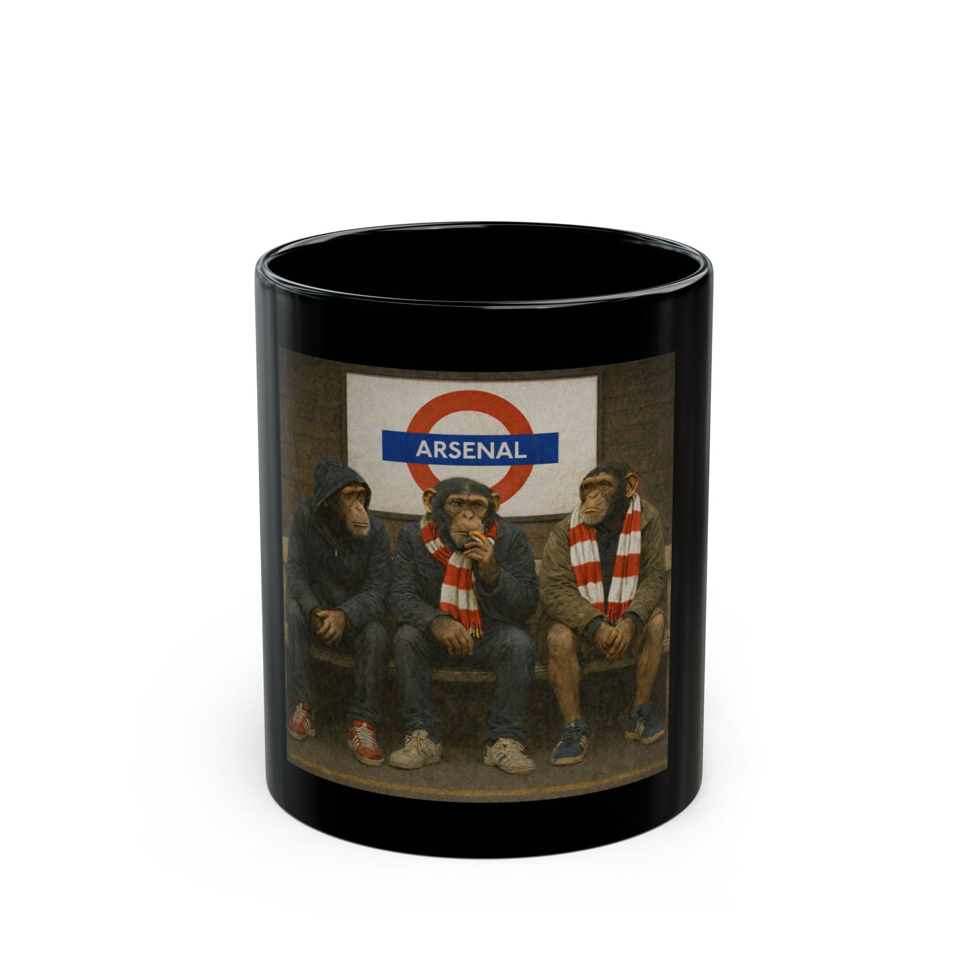 A black ceramic coffee mug featuring a detailed graphic print from On The Terrace showing three chimpanzees dressed as football casuals in retro trainers and red-and-white striped scarves, sitting on a London Underground bench under an Arsenal tube station sign.