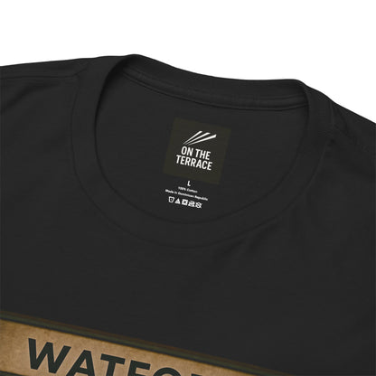 A black heavy cotton t-shirt flat lay from the file Front 2 (20).png, showing a square graphic print of three chimpanzees dressed as football casuals in retro trainers and a yellow, red, and black Watford scarf, sitting on a station bench under a Watford sign.