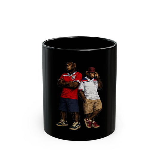 The cup shows an 11oz black ceramic mug featuring a graphic of two chimpanzees dressed in vintage England football casual attire. The monkey on the left is wearing a retro red away kit with dark blue shorts and navy trainers. The monkey on the right wears a vintage white home kit, a maroon cap, tan shorts, and red terrace-style trainers. Both characters stand against a solid black background.