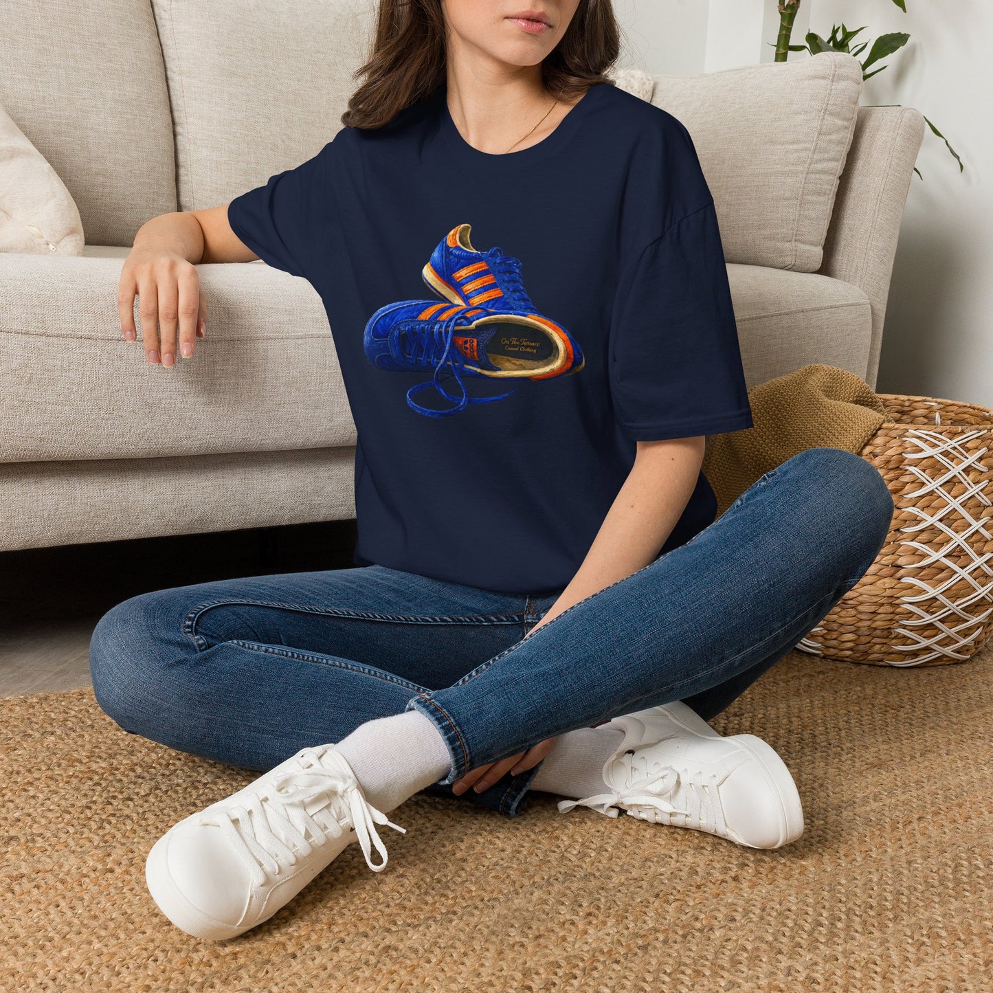 Person wearing a Navy t-shirt with hand-illustrated blue and orange retro terrace trainer sneaker graphic print, On The Terrace casual clothing brand
.