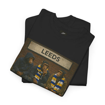 A folded black Leeds t-shirt with a graphic print of three chimpanzees wearing Leeds United scarves under a sign reading 'LEEDS', shown on a white background.