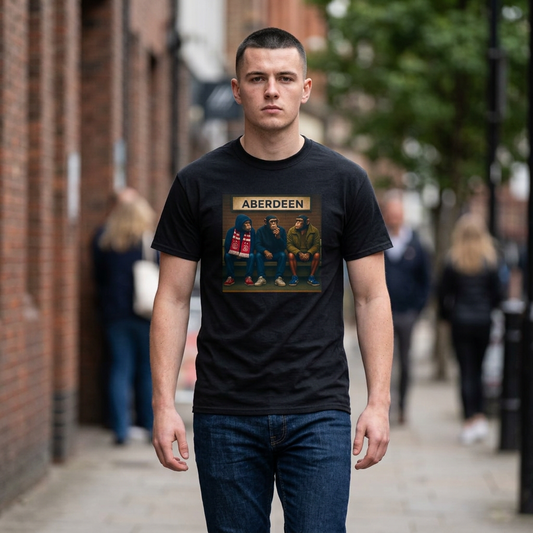 A man standing on a city sidewalk wearing a black graphic Aberdeen t-shirt with a vintage-style print of the band Aberdeen and the word 'ABERDEEN' on the chest, paired with dark blue jeans.
