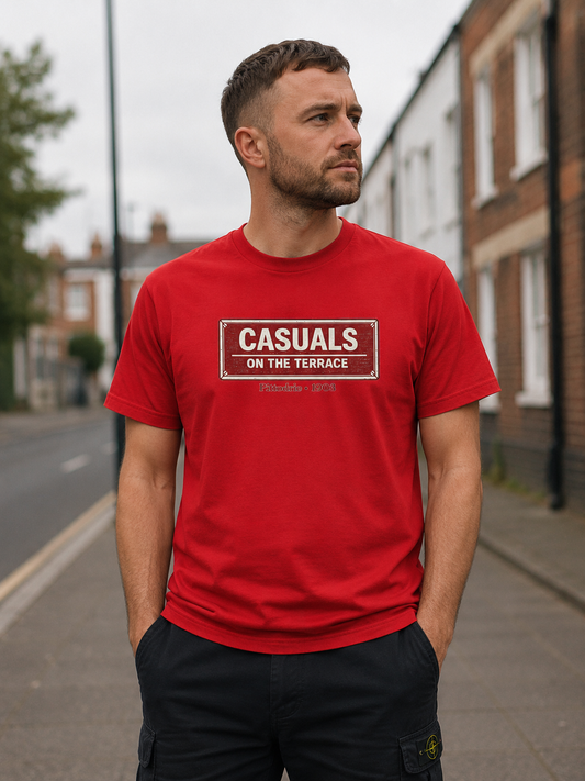 A man wearing a red heavy cotton Aberdeen t-shirt flat lay featuring a central vintage red and white street sign graphic reading "CASUALS ON THE TERRACE" with "Pittodrie • 1903" printed below, and an inner neck label for On The Terrace. He is standing on a residential street.
