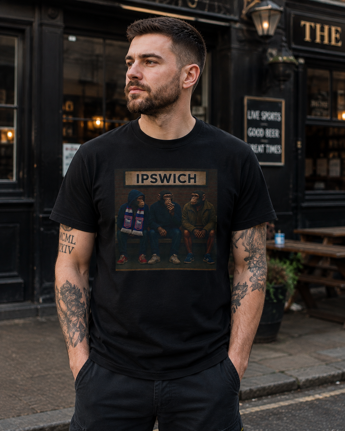 A man wearing a black Ipswich t-shirt with a 'IPSWICH' band print, standing on a street in front of a dark pub.