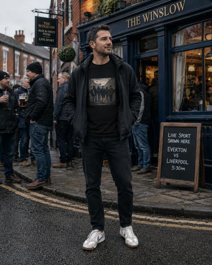 A man wearing a black Northern Monkey graphic t-shirt under a black zip-up hoodie and black jeans stands on the street in front of 'The Winslow' pub. He is wearing white sneakers.