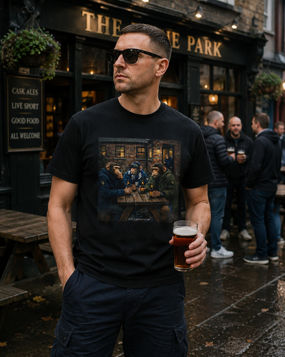 A man wearing a black Northern Monkey graphic t-shirt with a detailed print of a pub scene, standing outside 'The Park' pub and holding a pint of beer.