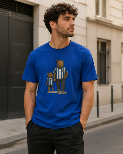 A man wearing a royal blue crewneck SWFC t-shirt with a graphic of two teddy bears in blue and white striped jerseys, standing on a city street.