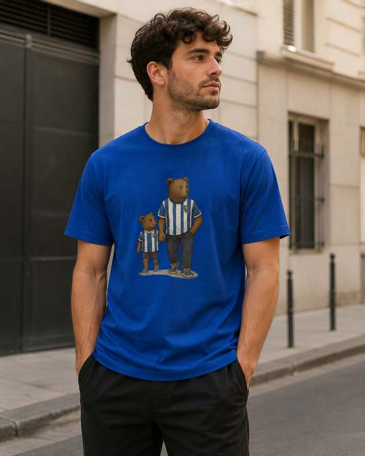 A man wearing a royal blue crewneck SWFC t-shirt with a graphic of two teddy bears in blue and white striped jerseys, standing on a city street.