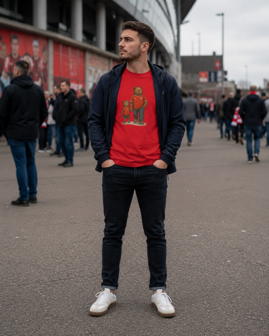 A man wearing a red Arsenal graphic t-shirt under an open navy blue hoodie, paired with dark jeans and white sneakers, standing in a crowded outdoor street setting.