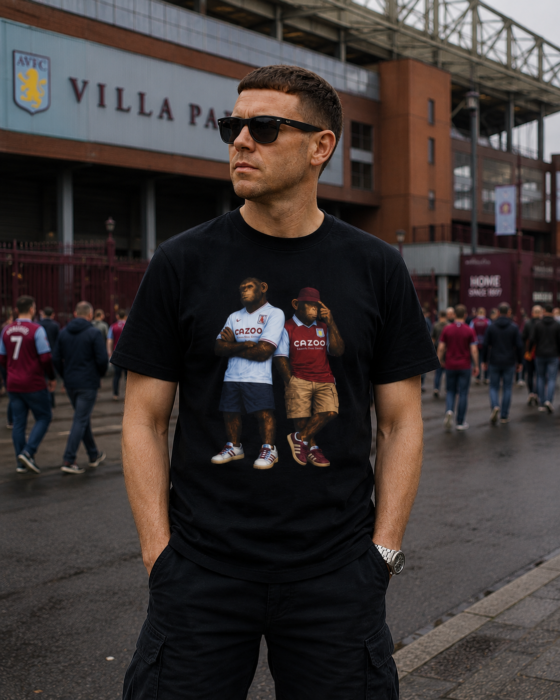 A man wearing a black Aston Villa  graphic t-shirt with a print of two football players in Aston Villa jerseys, standing outside Villa Park stadium.