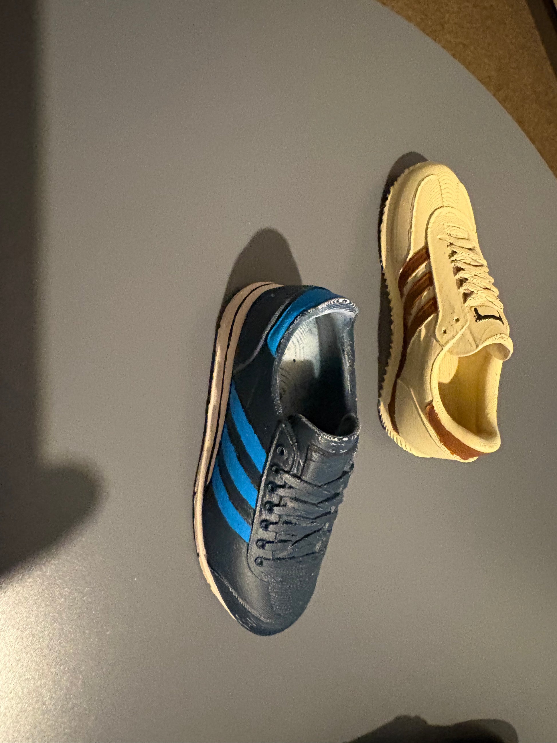 Blue and beige sneakers with three stripes on a grey surface, casual sports shoe design