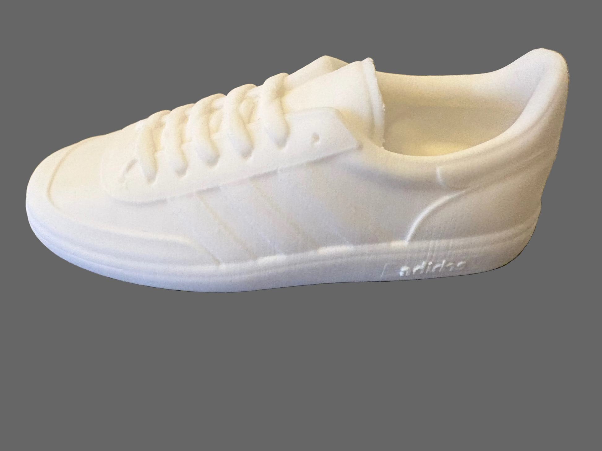 White Adidas manchester sneaker on a textured gray surface