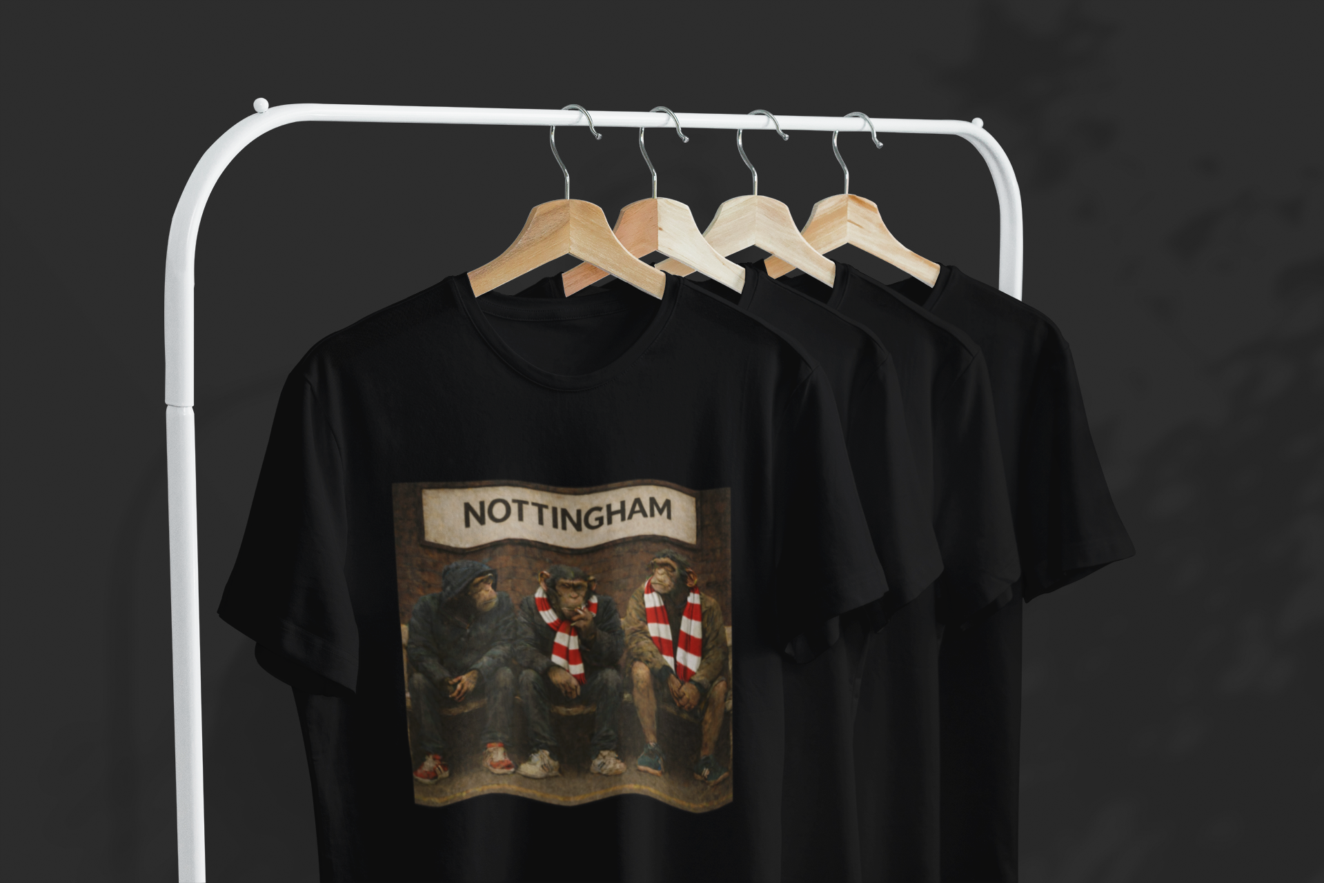 A black short-sleeve Notts Forest T-shirt hanging on a wooden hanger from a white clothing rack, featuring a large graphic print of the band Nottingham on the front. Three more black shirts are visible behind it on the rack against a dark gray background.