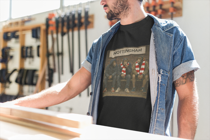 A man wearing a black graphic Notts Forest t-shirt with a Nottingham print, layered under an open blue denim shirt, standing in a workshop environment.