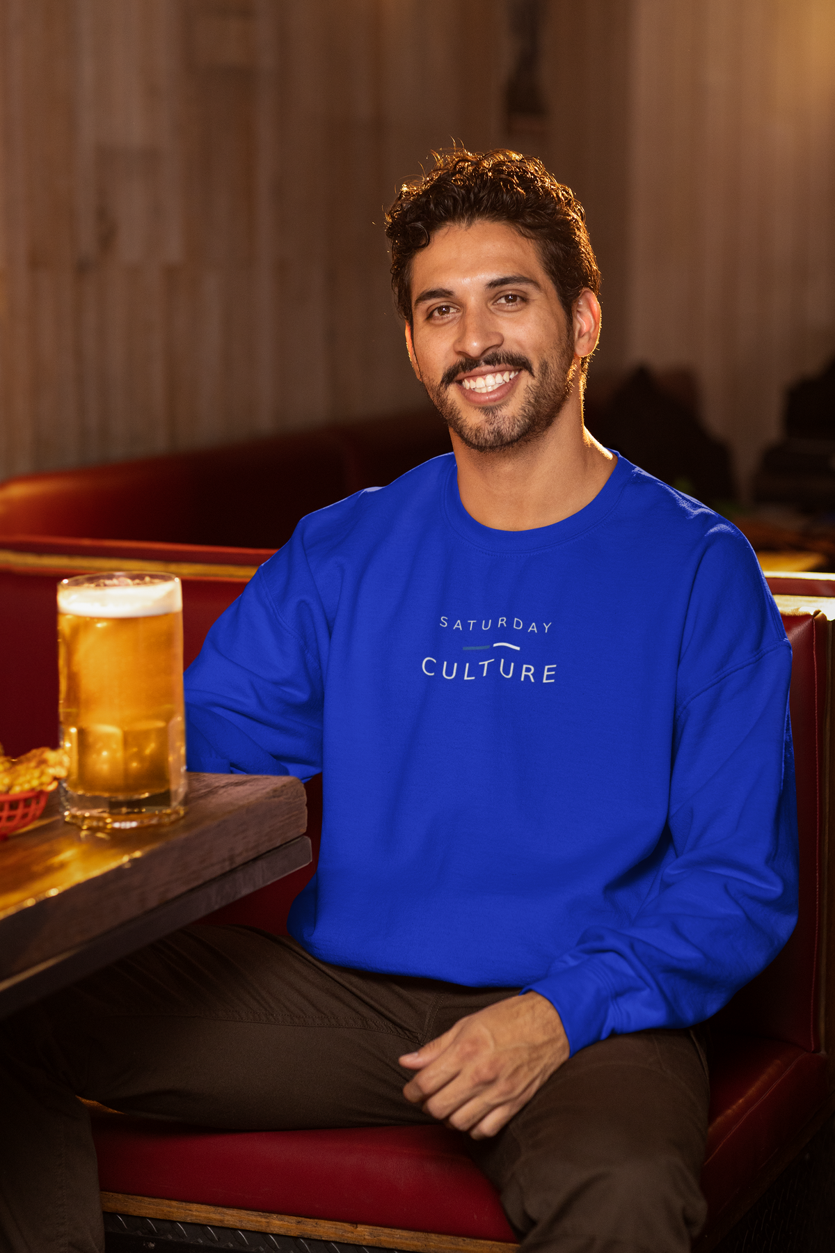 Man in a pub with a pint wearing the royal blue Saturday Culture football casuals sweatshirt