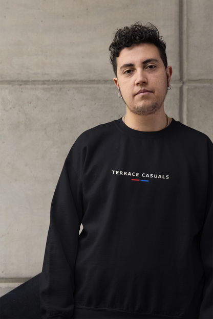 Man leaning on a wall wearing the black Terrace Casuals embroidered sweatshirt