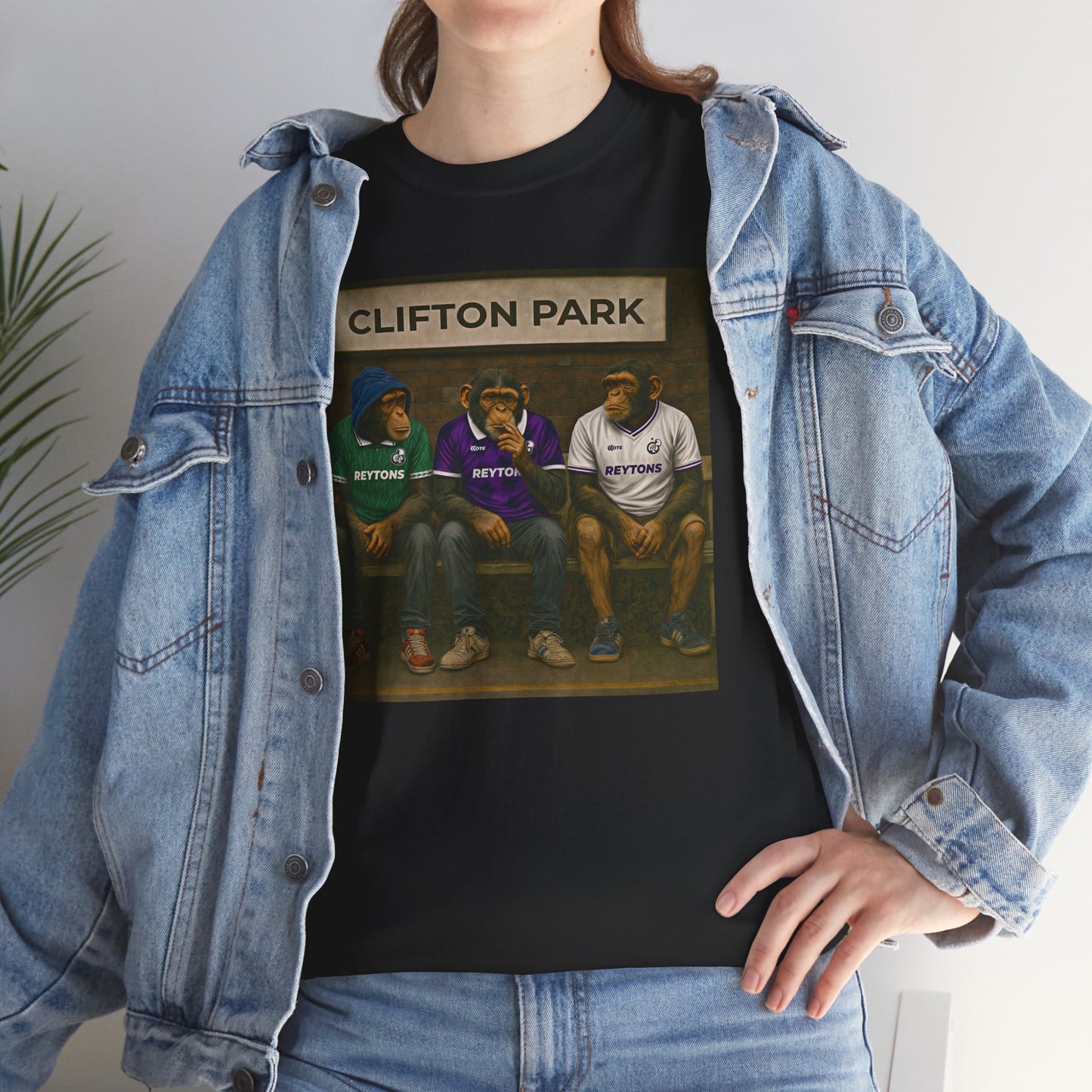 A person wearing a black graphic Reytons T-shirt with a 'Clifton Park' sports illustration, layered under an open light-wash denim jacket and paired with blue jeans.