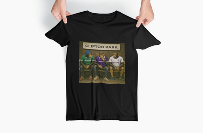 A black short-sleeve Reytons t-shirt held up by two hands against a light gray background. The shirt features a rectangular graphic print in the center depicting three men sitting on a bench in front of a sign that reads 'CLIFTON PARK'.