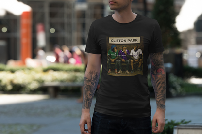 A man wearing a black graphic Reytons t-shirt with a 'Clifton Park' sports illustration on the front, standing in a blurred outdoor park setting.