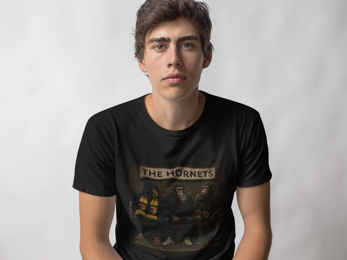 A young man wearing a black Watford t-shirt with a vintage-style graphic of hockey players and the text 'THE HORNETS' on the front, set against a plain light gray background.