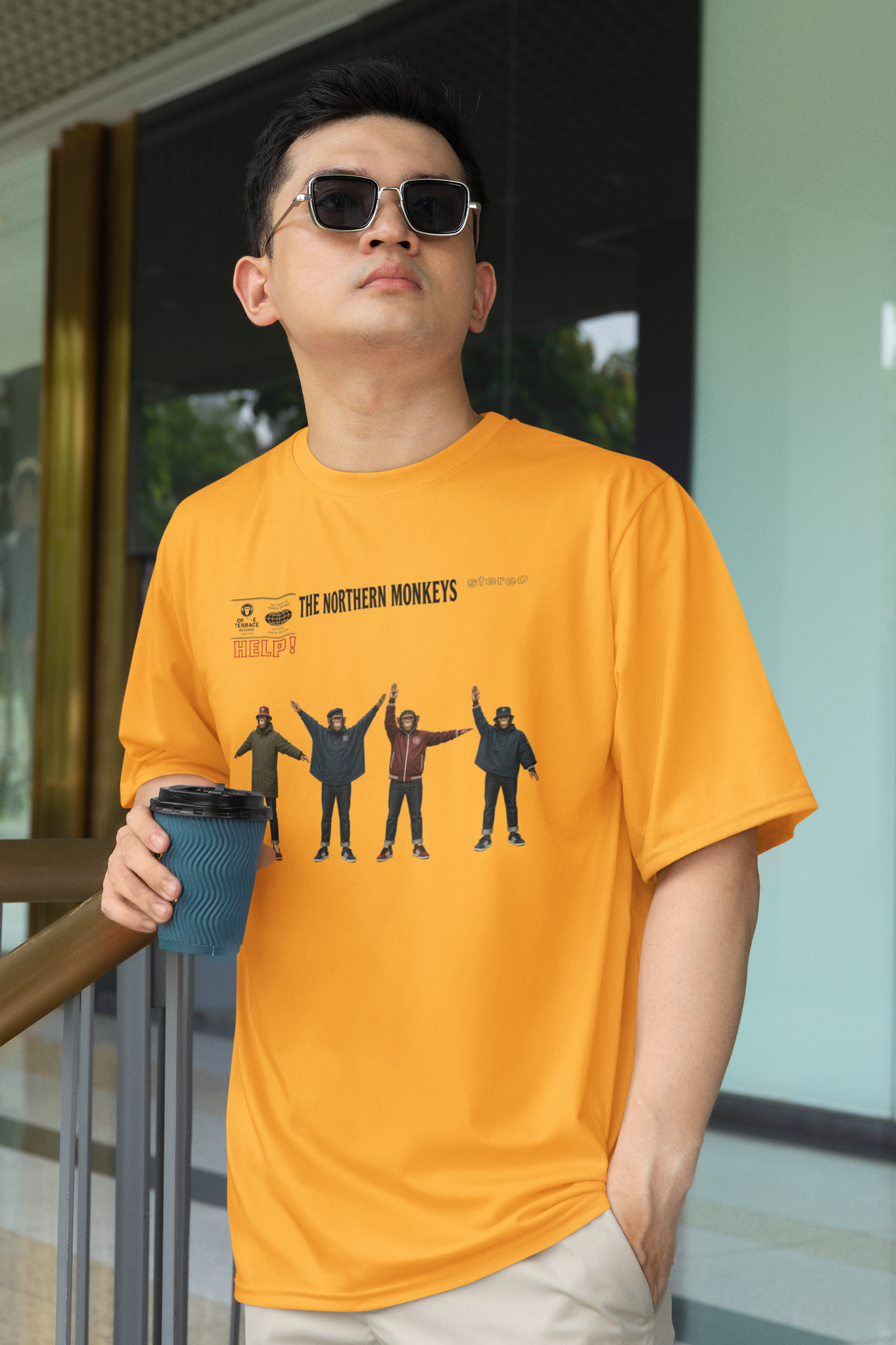 Man in sunglasses modelling mustard Beatles Help Casuals T-shirt while holding a drink