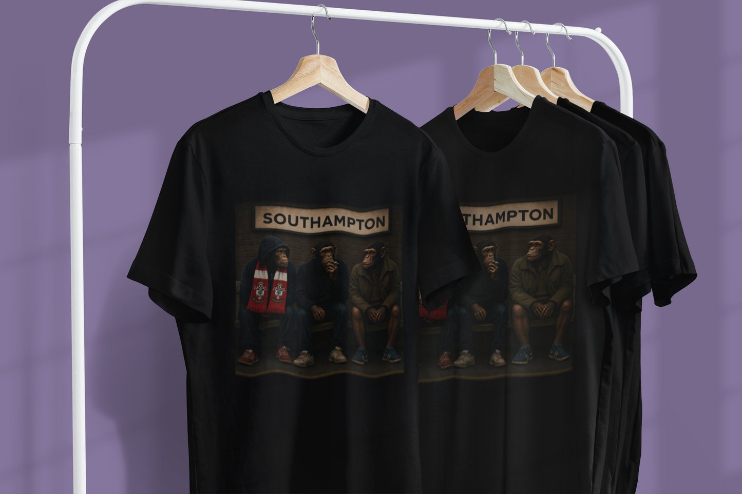Black short-sleeve graphic Southampton t-shirts hanging on wooden hangers from a white clothing rack against a solid purple wall. The shirts feature a rectangular graphic print depicting the band Southampton seated on a bench under a sign reading 'SOUTHAMPTON'.