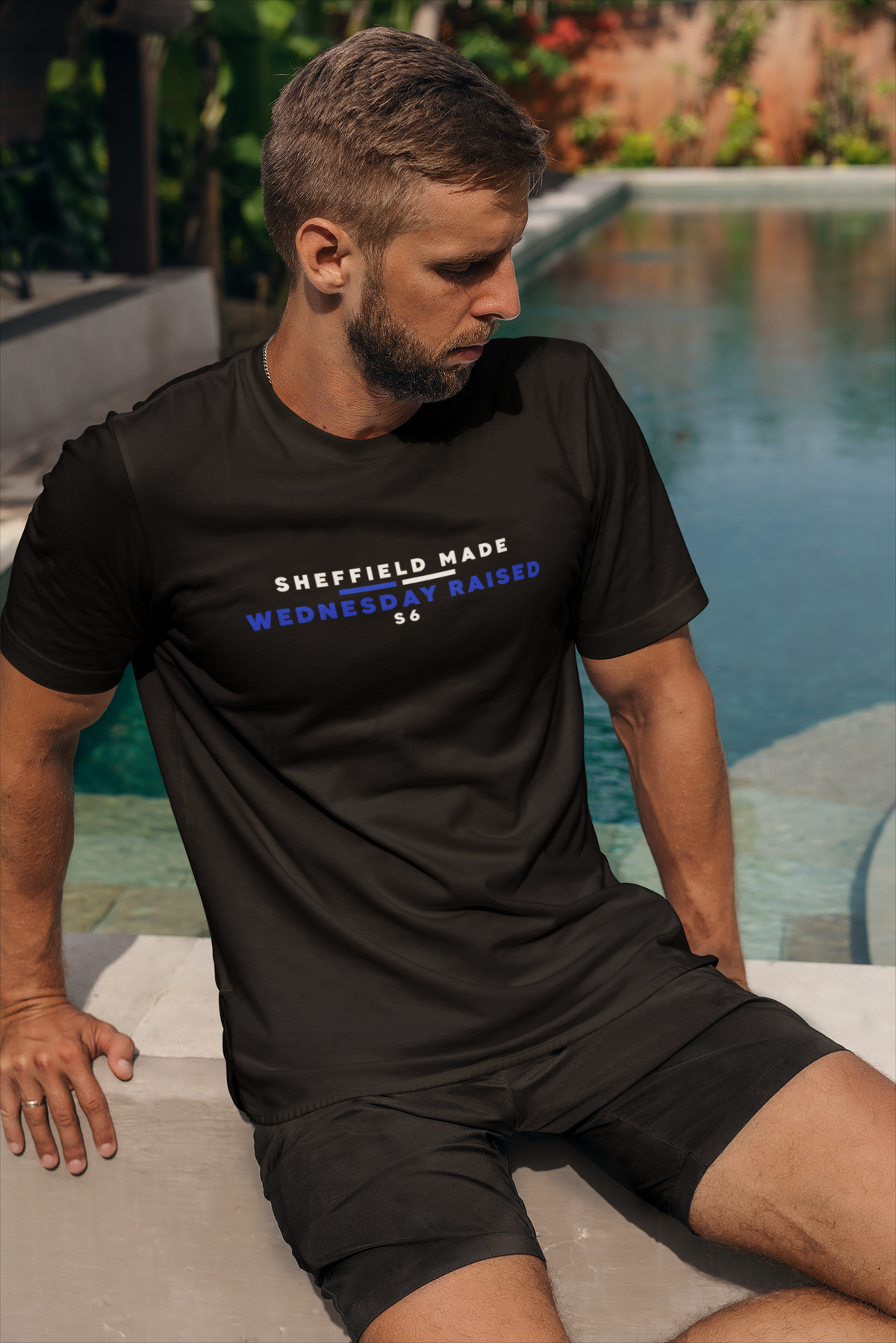 Bearded man sitting by a pool wearing black Sheffield Wednesday slogan tee