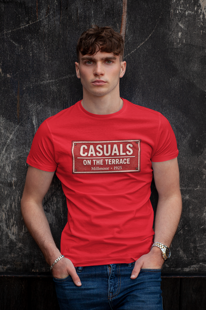 A man wearing a bright red Rotherham t-shirt with a vintage-style graphic that reads 'CASUALS ON THE TERRACE' in beige, posed against a dark textured wall.