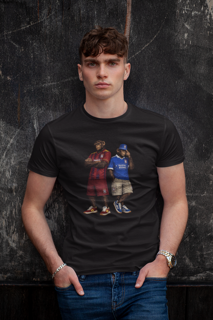 A man wearing a black Ipswich t-shirt with a graphic print of two men in streetwear, posed against a dark textured wall.