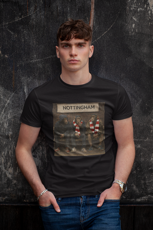 A man wearing a black graphic Notts Forest t-shirt with a 'NOTTINGHAM' football club print, paired with blue jeans, standing against a dark textured wall.