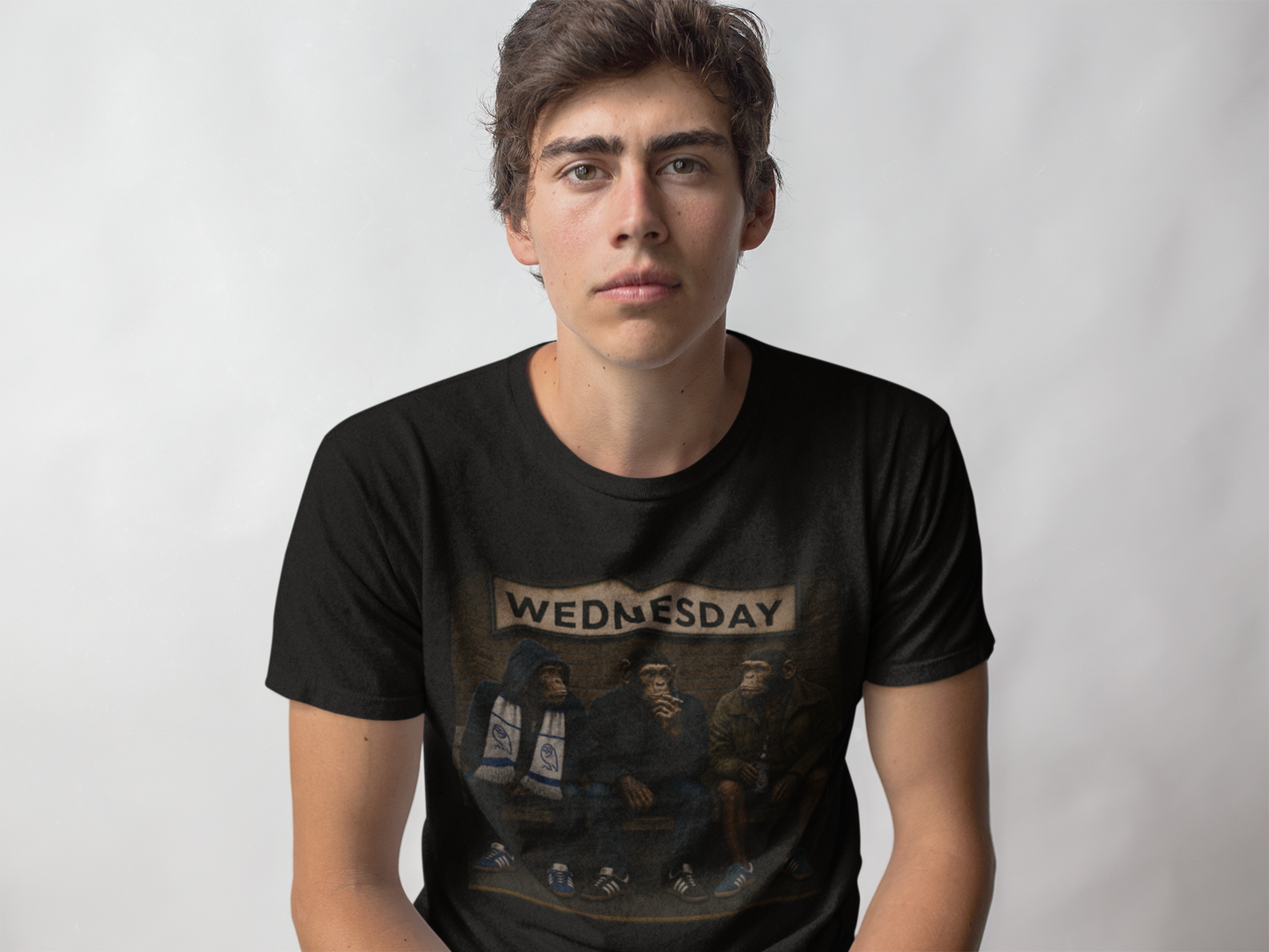 A young man wearing a black graphic swfc t-shirt with a vintage-style illustration and the word 'WEDNESDAY' printed across the chest, set against a plain light gray background.