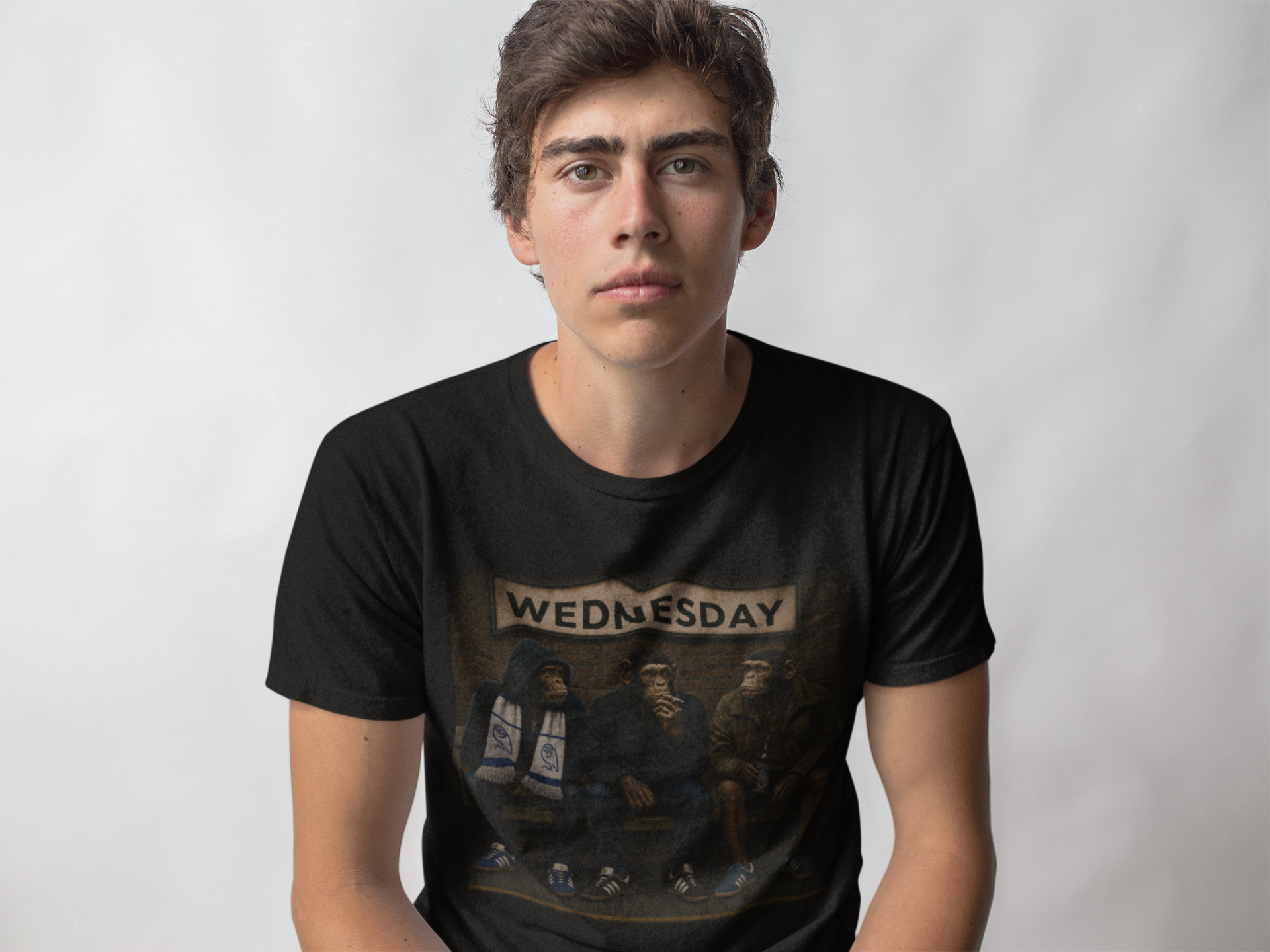 A young man wearing a black graphic swfc t-shirt with a vintage-style illustration and the word 'WEDNESDAY' printed across the chest, set against a plain light gray background.