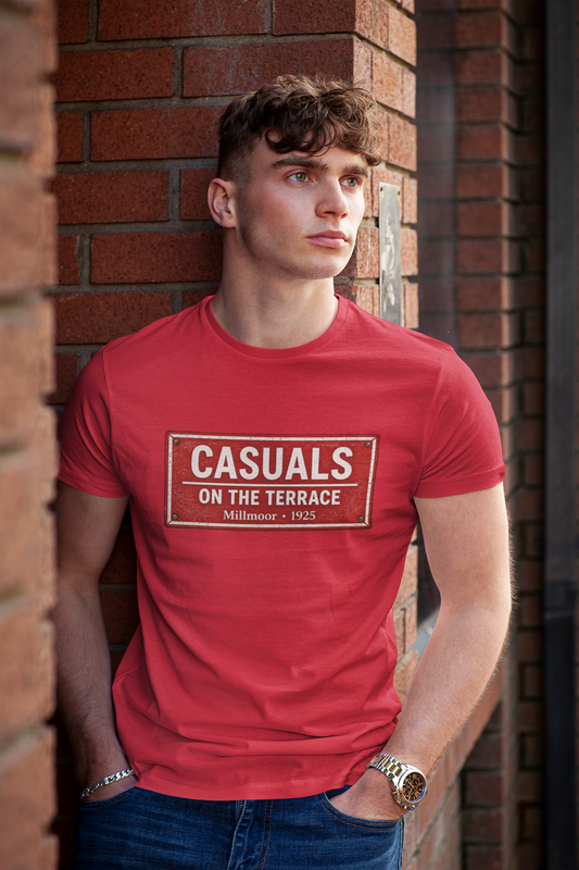 A young man wearing a red Rotherham t-shirt with a white and black 'CASUALS ON THE TERRACE Millmoor 1923' print, leaning against a red brick wall.